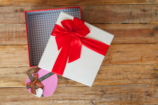 White gift box and red ribbon and mini heart inside on wood background with space.