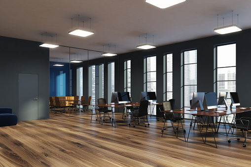 Open space office corner with gray and glass walls, a wooden floor and narrow windows. Rows of computer desks and a conference room. 3d rendering mock up