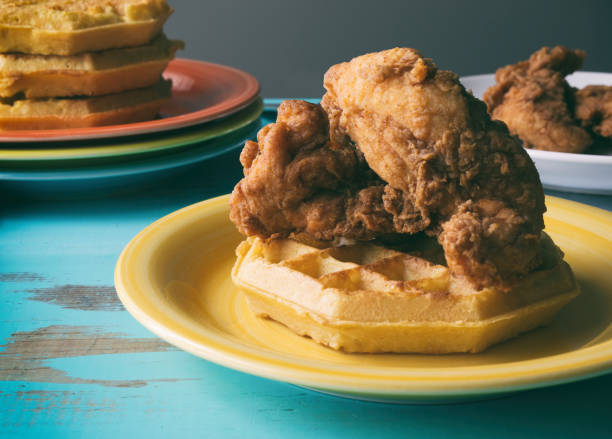 pollo frito y waffles descansando sobre una rústica mesa azul turquesa. multi color placas en el fondo. - waffle chicken fried chicken food fotografías e imágenes de stock