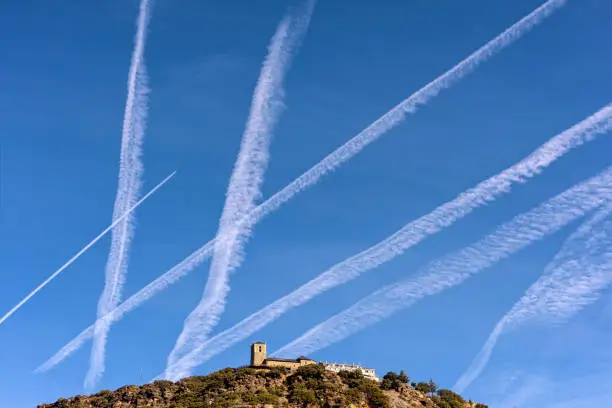 Many chem trails mark flight paths on northern Spain blue sky.