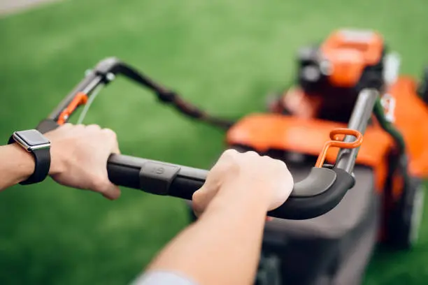 A man holds a lawn mower for the handle. He came to the tools store for gardening. He has a wristwatch on his hand.