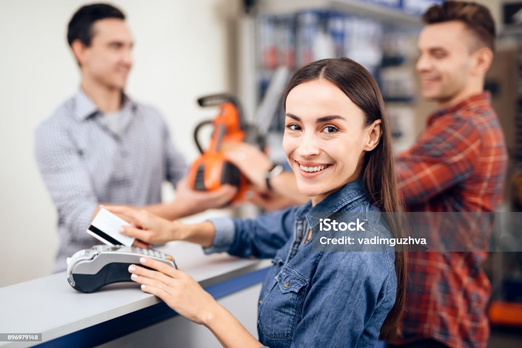 The guy and the girl pay for the purchase of a chainsaw. The guy and the girl pay for the purchase of a chainsaw. They are in the shops of tools for gardening. They use a credit card. Hardware Store Stock Photo