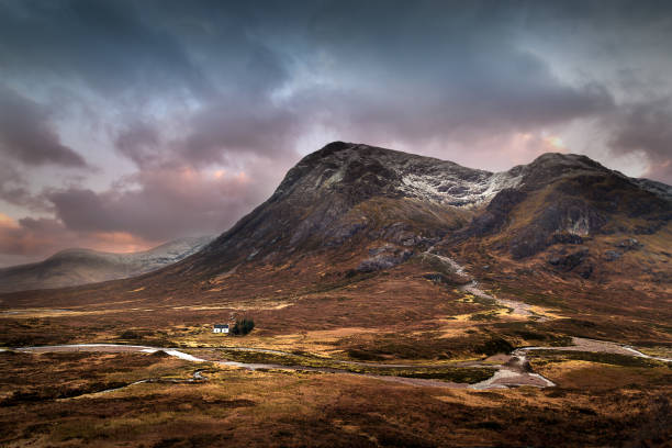 Glencoe, Scotland, UK A small house nestles in the valley beneath a snow capped mountain in Glencoe. A river runs through the scene. It is wild and remote scottish highlands stock pictures, royalty-free photos & images