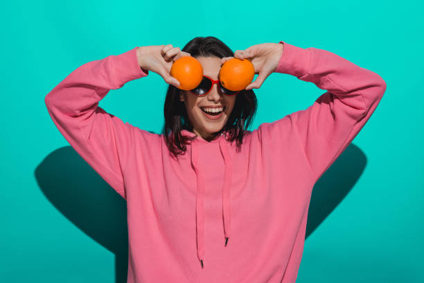istock Young woman holding an orange while standing by a blue color background 897017942