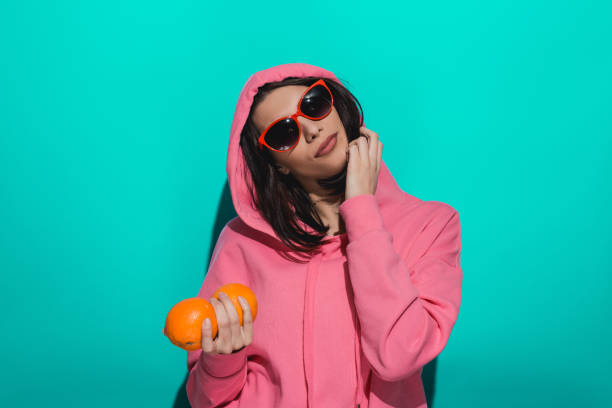 istock Young woman holding an orange while standing by a blue color background 897020504