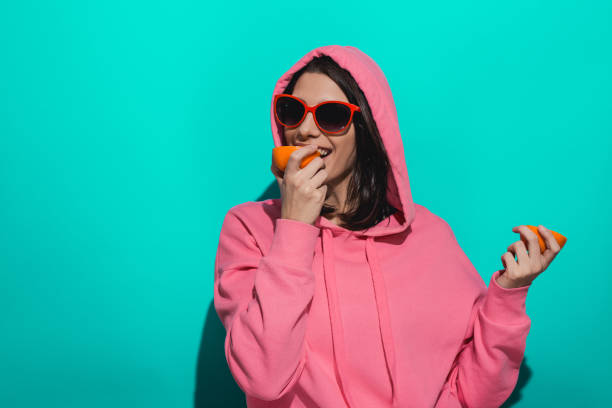istock Young woman holding an orange while standing by a blue color background 897020832