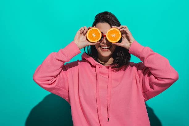 istock Young woman holding an orange while standing by a blue color background 897020950