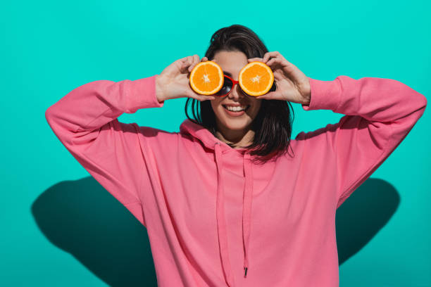 istock Young woman holding an orange while standing by a blue color background 897020952