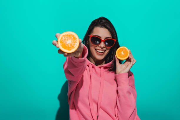 istock Young woman holding an orange while standing by a blue color background 897023042