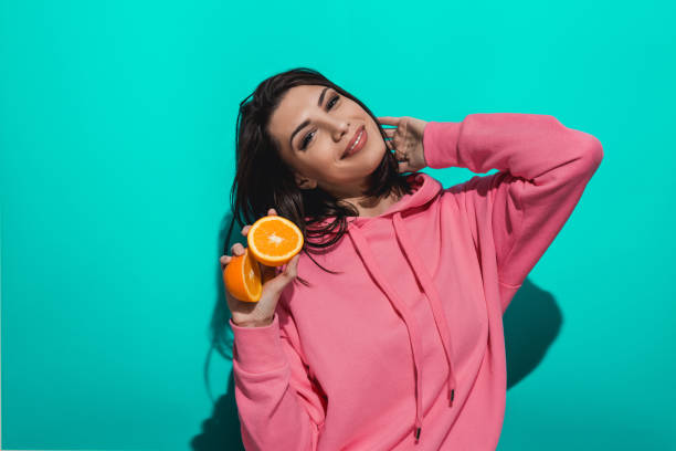istock Young woman holding an orange while standing by a blue color background 897023330