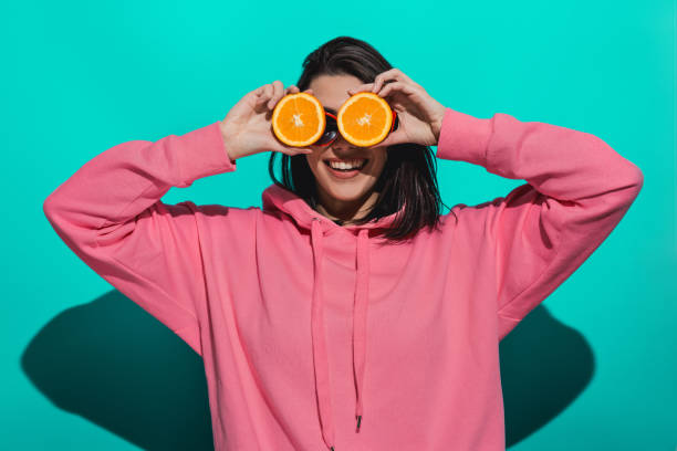 istock Young woman holding an orange while standing by a blue color background 897023402