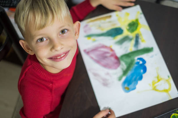 istock Cute little boy looking at camera and paint with watercolors 897026296