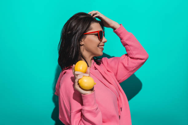 istock Young woman holding lemon while standing by a blue color background 897027342