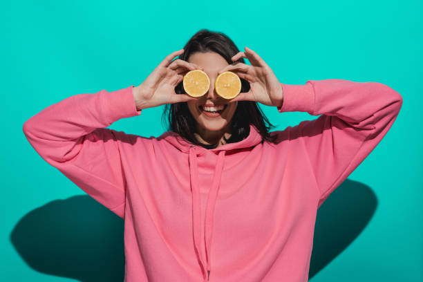 istock Young woman holding lemon while standing by a blue color background 897030238