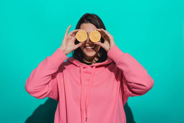 istock Young woman holding lemon while standing by a blue color background 897030244