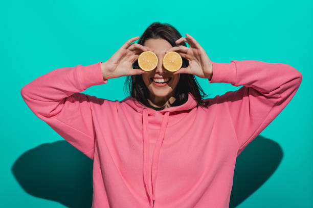Young woman holding lemon while standing by a blue color background