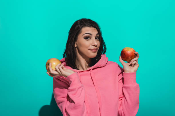 istock Young woman holding an apple while standing by a blue color background 897039076