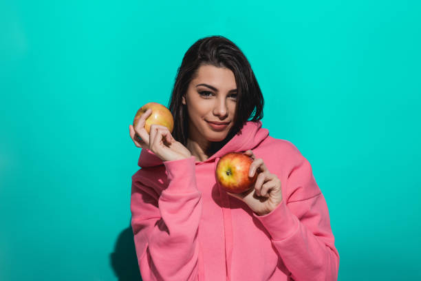istock Young woman holding an apple while standing by a blue color background 897039212