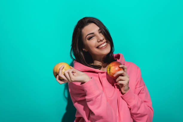 istock Young woman holding an apple while standing by a blue color background 897039444