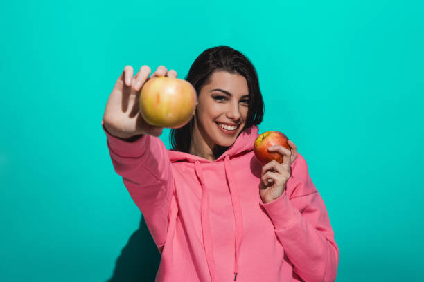 istock Young woman holding an apple while standing by a blue color background 897039456