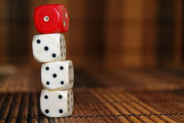 istock Stack of three white plastic dices and one red dice on brown wooden board background. Six sides cube with black dots. Number 1, 3, 4, 5 897040086