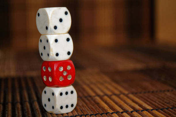 istock Stack of three white plastic dices and one red dice on brown wooden board background. Six sides cube with black dots. Number 3, 4, 5, 6 897040200