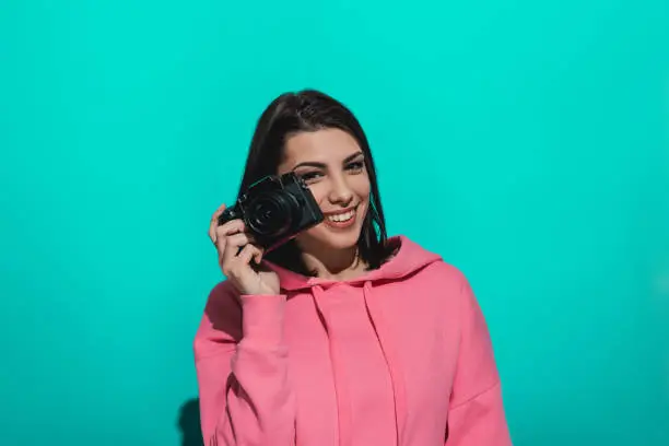 Photo of Young woman holding a camera while standing by a blue color background