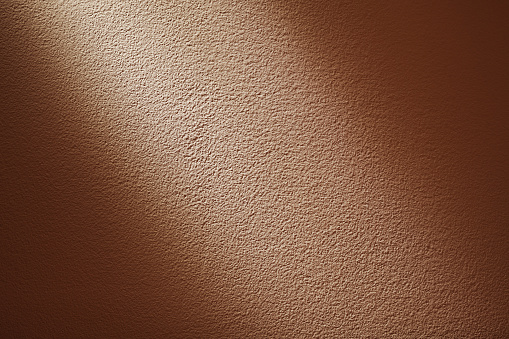 Closeup view of pale orange wall, partly illuminated, details of texture.