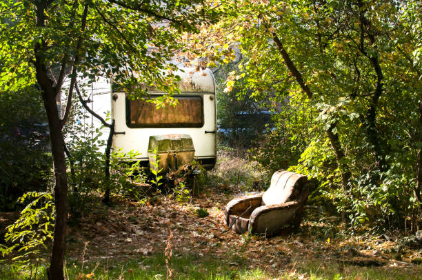 Old vintage abandoned grunge caravan and shabby armchair in overgrown with vegetation place