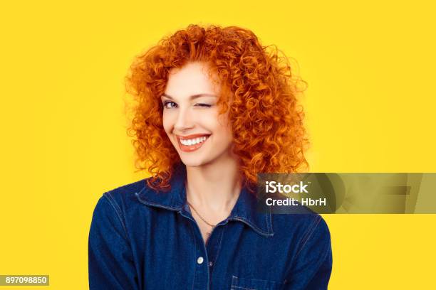 Winking Closeup Woman Redhead Curly Hair Smiling Blinking Eye To You Camera Isolated On Yellow Background Happy Life Pictures Happiness Stock Photo - Download Image Now