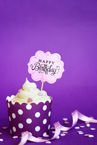 Cupcake with small decorative hearts and happy birthday sign, against violet background