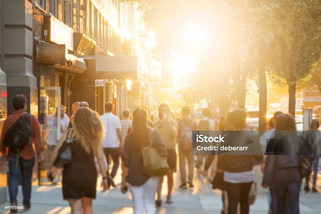 Crowd of people walking down sidewalk in Manhattan, New York City Crowd of anonymous men and women walking down an urban sidewalk with bright glowing sunlight in the background on a busy street in downtown Manhattan, New York City People Stock Photo