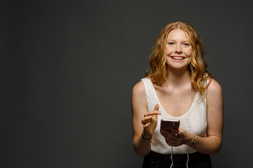 Young redhead millennial teenage girl listening to music on her phone photographed in studio