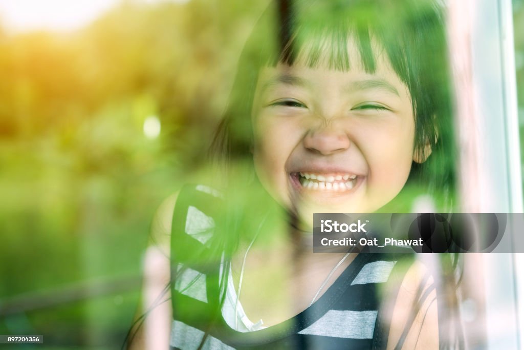 Asian child girl standing on glass mirror reflecting green forest. She was smiling in a good mood. Asia Stock Photo