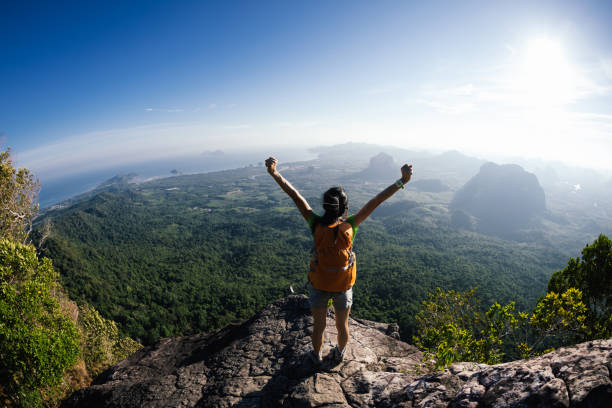 istock cheering young woman with backpacker enjoy the view on mountain top cliff edge 897207046