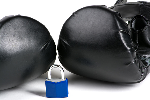 Concept and idea of security, protection with two black boxing gloves behind a blue padlock on white background.