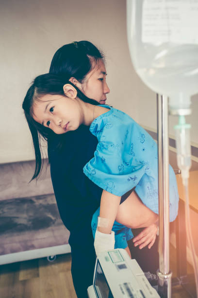 Asian mother carrying and take care her daughter in hospital, saline intravenous (IV) drip on child's patient hand. Girl feeling sad and looking away. Health care stories. Vintage film filter effect.