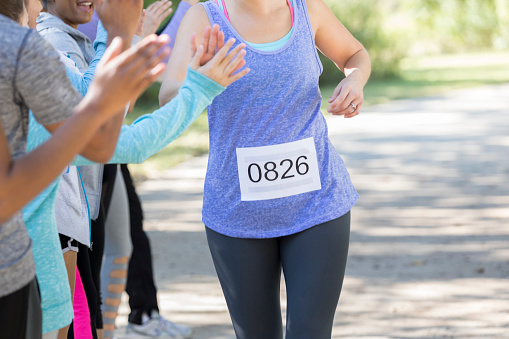 An unrecognizable woman wearing a sports bib high fives a row of people as she runs to the finish line of a charity race.