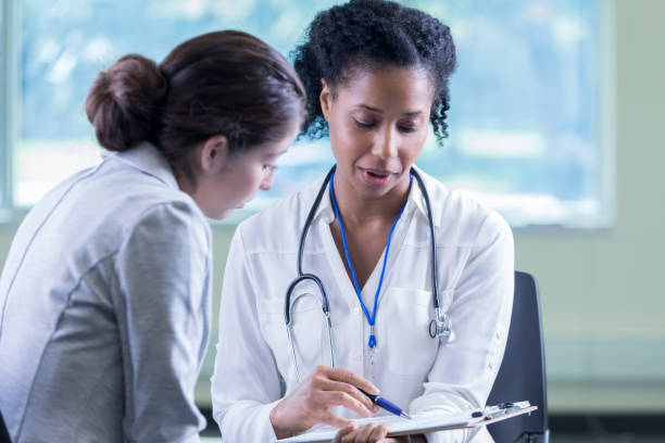 Doctor reviews a patient's medical information Confident female doctor reviews a patient's medical information. The doctor is pointing to something on the patient's medical forms. The doctor is wearing a stethoscope. medical insurance stock pictures, royalty-free photos & images