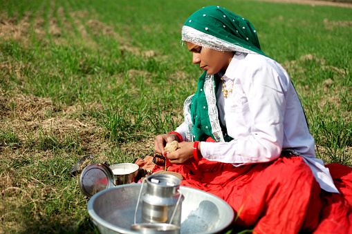Female farmer of Indian ethnicity sitting in the green field & eating lunch.