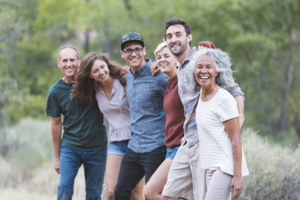 Friends of All Ages A multiethnic group of friends embrace and smile toward the camera. They're lined up loosely and desert vegetation and sagebrush are in the background. adult age stock pictures, royalty-free photos & images