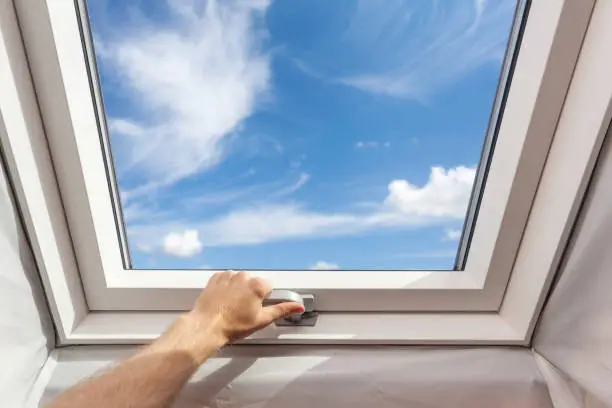 Photo of Man close new skylight (mansard window) in an attic room against blue sky