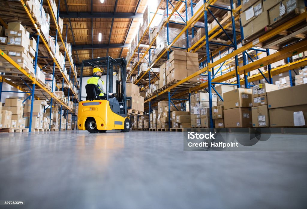 Warehouse man worker with forklift. Young male worker lowering a pallet with boxes. Forklift driver working in a warehouse. Warehouse Stock Photo