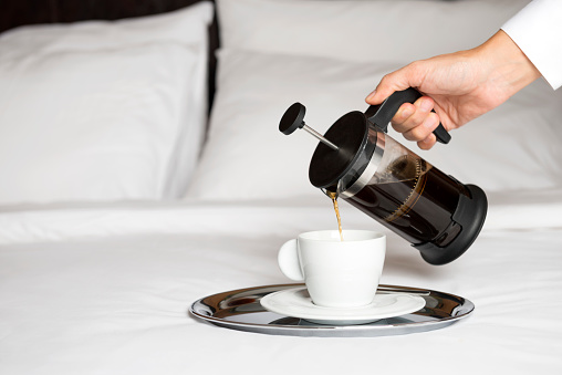 French press coffee on bed in hotel room.