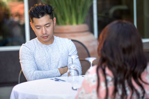 Interracial Date with Asian Man Handsome asian man on an outdoor date with a black female.  The couple are sitting in a restaurant or cafe setup for speed dating.  He looks bored and disappointed. blind date stock pictures, royalty-free photos & images