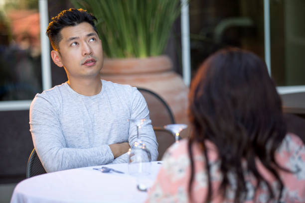 Interracial Date with Asian Man Handsome asian man on an outdoor date with a black female.  The couple are sitting in a restaurant or cafe setup for speed dating.  He looks bored and disappointed. blind date stock pictures, royalty-free photos & images