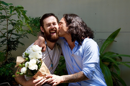 Diverse friends at a celebration giving a kiss on the cheek and receiving flowers