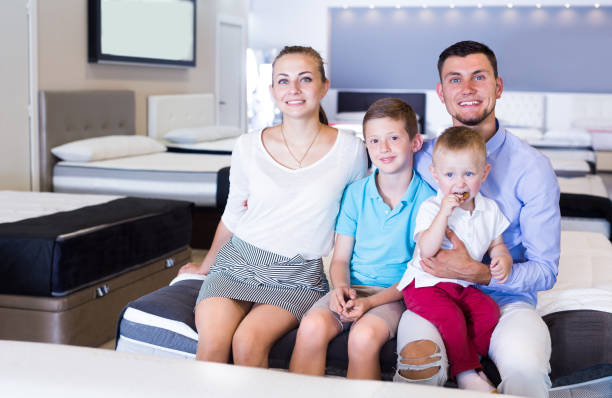 istock Young cheerful family sitting on bed in store 897319352