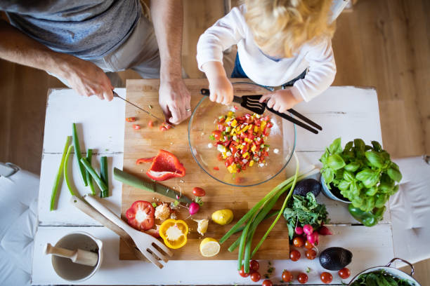 Young father with a toddler boy cooking. Unrecognizable father with a toddler boy cooking. A man with his son making vegetable salad. Top view. preparing food stock pictures, royalty-free photos & images