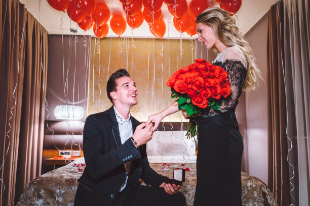 Sentimental young woman hugging her boyfriend or sweetheart as she smiles tenderly down at a single red rose he has just given her, symbolic of love and romance or Valentines Day, multiracial couple